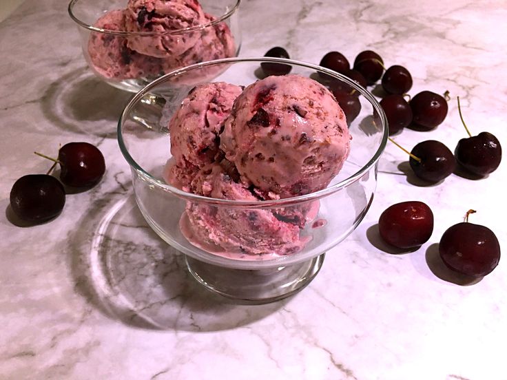 two bowls filled with ice cream next to cherries on a marble counter top,