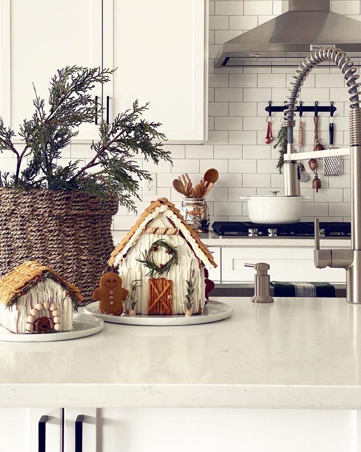 two small gingerbread houses on plates in a kitchen with white cabinets and countertops