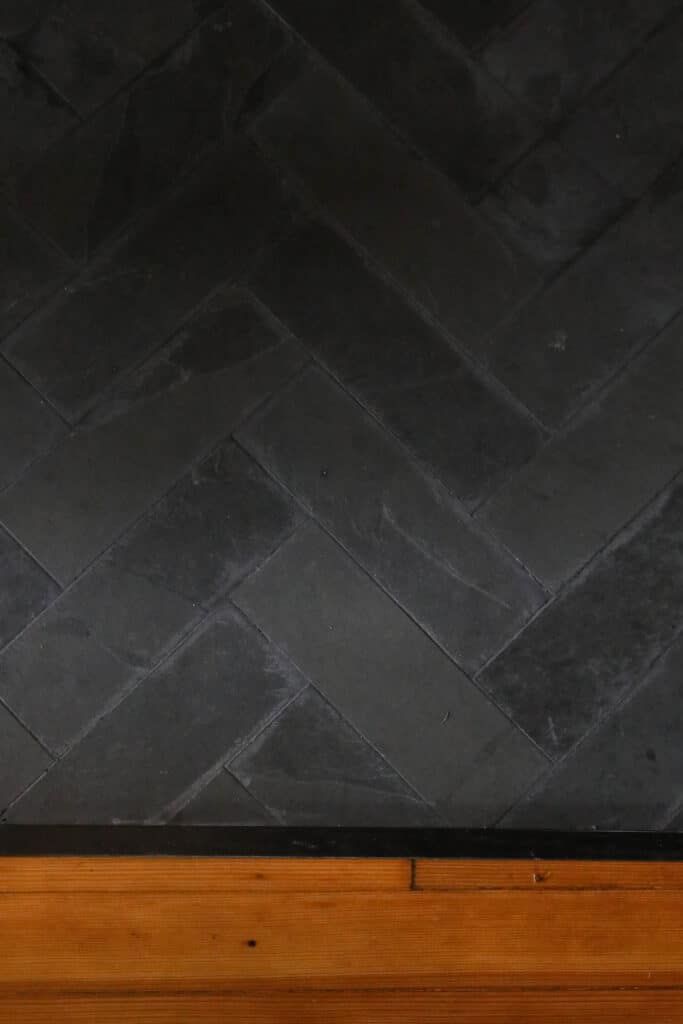 a cat sitting on top of a wooden bench next to a black tile flooring