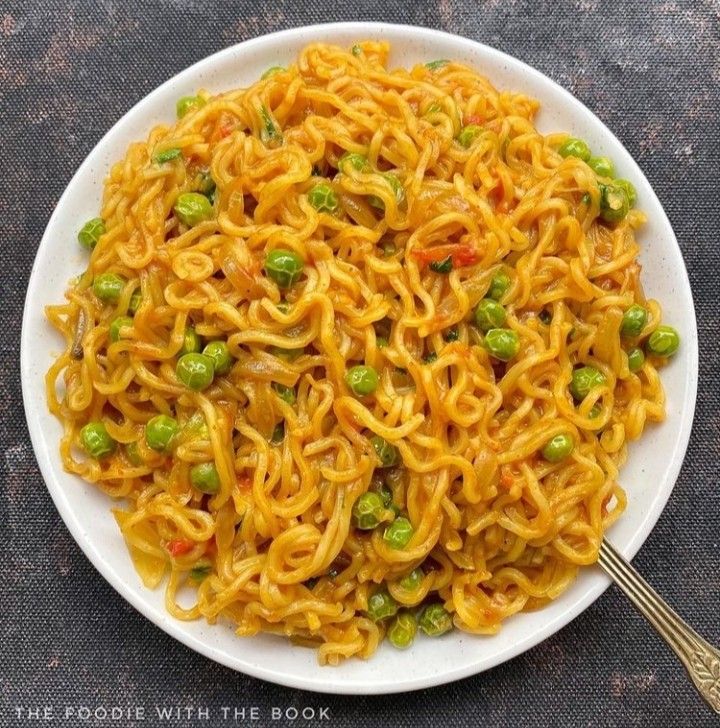 a white plate filled with noodles and peas on top of a table next to a fork