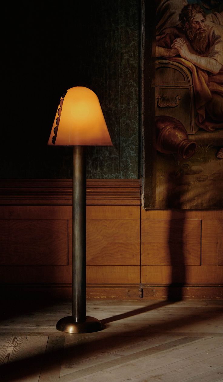 a lamp that is sitting on top of a wooden floor in front of a painting