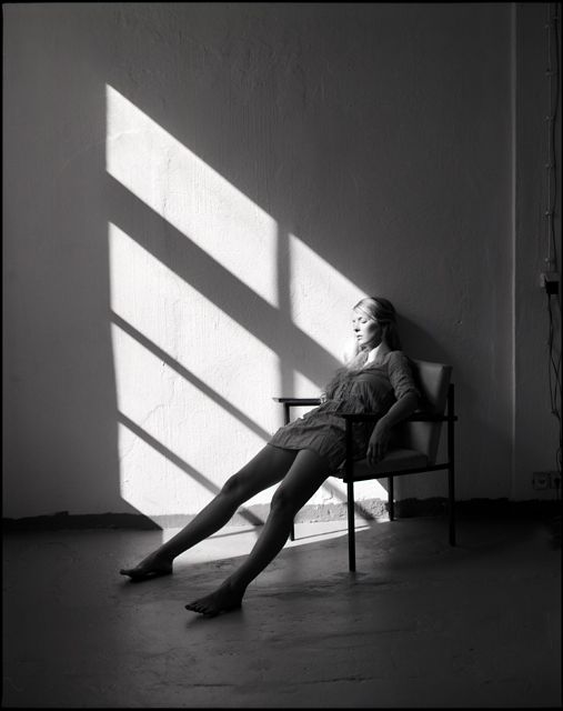 a woman sitting in a chair next to a wall with the sun shining through it