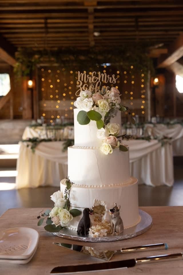 a wedding cake with white flowers and greenery on top is sitting on a table