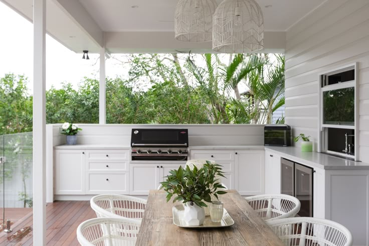 an outdoor kitchen with white cabinets and wooden table