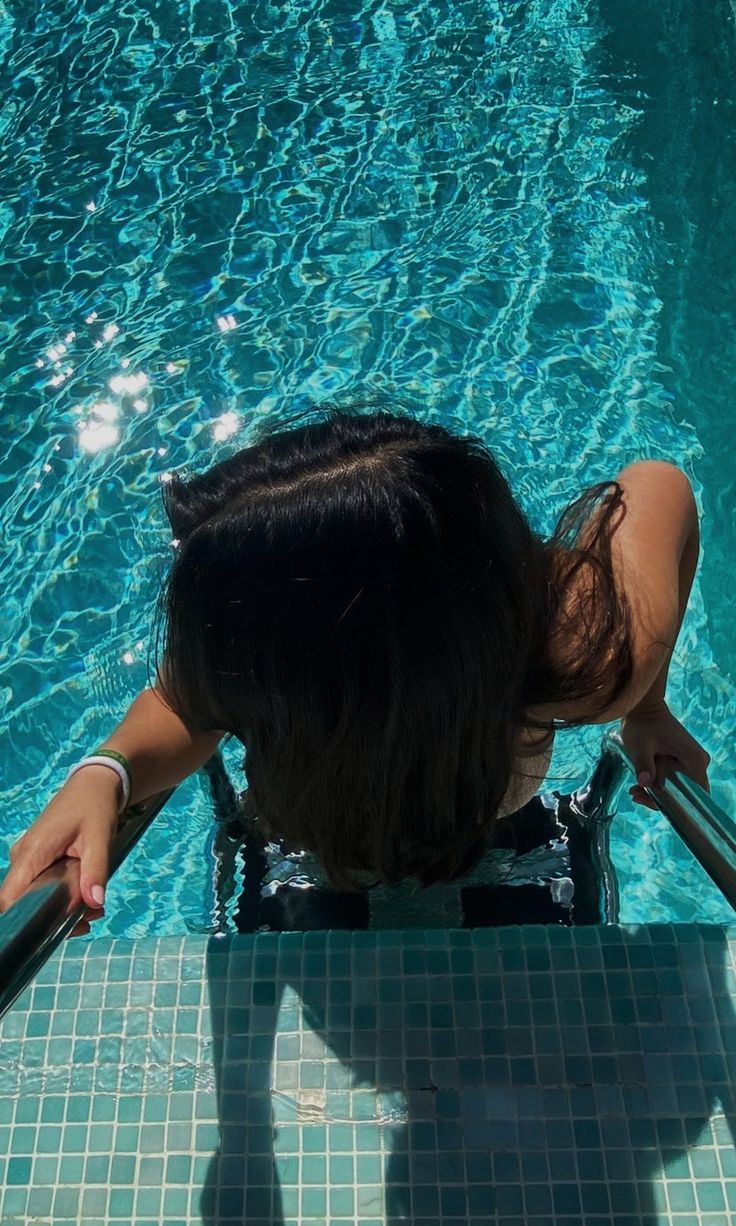 a woman sitting on the edge of a swimming pool with her back to the camera