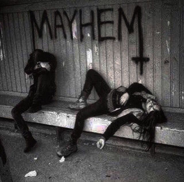 two people laying on the ground in front of a wall with graffiti that says mayhem