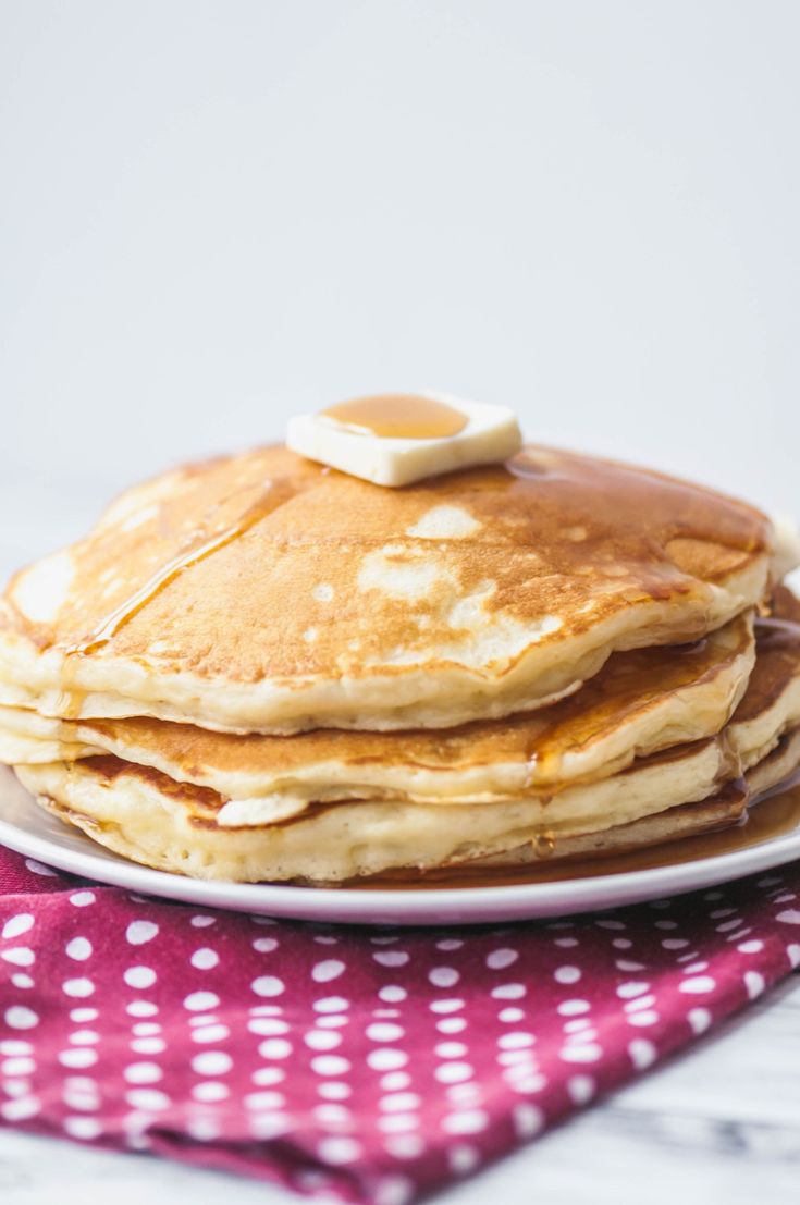 a stack of pancakes with butter on top sitting on a pink and white polka dot napkin