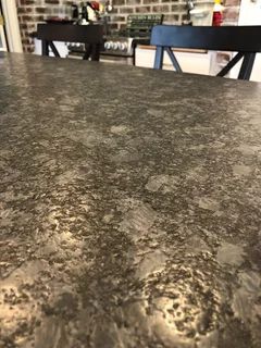 a kitchen counter top that has brown spots on it and black chairs in the background