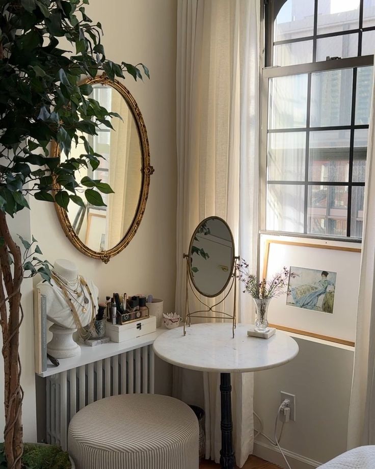 a room with a table, mirror and stool next to a plant in the corner