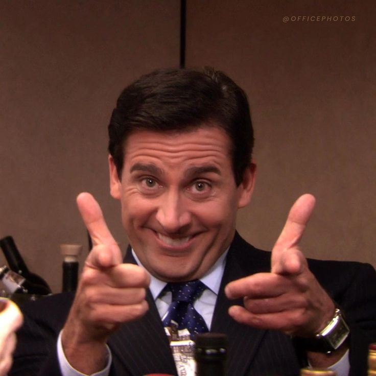 a man in a suit and tie giving the peace sign with two bottles behind him