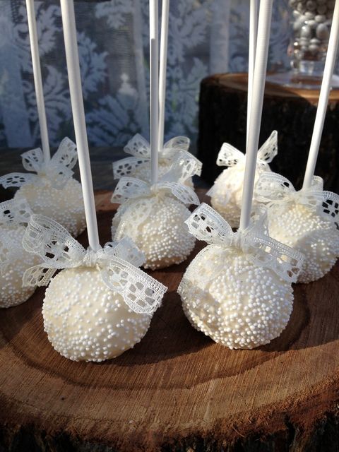 some white candles are sitting on top of a wooden slice with lace and bowknots