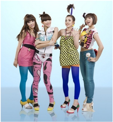 four young women are standing together in front of a blue background and one is holding a cell phone