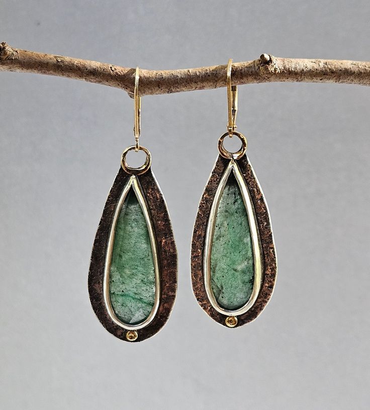 I was drawn to aventurine because of its wonderful rich green coloring. I love the mossy green inclusions and the subtle sparkle of mica. These tiny flecks of mica add depth and interest to the stone. These earrings are sawn out of sterling silver sheet that has been textured with a pebble pattern. The long-faceted drops of aventurine have been bezel set in fine silver. The backs of the earrings have been sawn out to allow light to enter from the back illuminating the stone. A disk of 18K gold a Elegant Untreated Green Jewelry, Elegant Hand Forged Green Jewelry, Elegant Green Hand-forged Jewelry, Hand Forged Green Teardrop Jewelry, Green Hand Forged Jewelry For Anniversary, Untreated Green Teardrop Jewelry, Hand Forged Green Drop Earrings, Green Artisan Pierced Earrings, Green Moss Agate Earrings For Gift