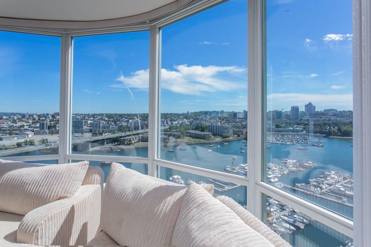 a living room filled with white furniture and large windows overlooking the cityscape in the distance