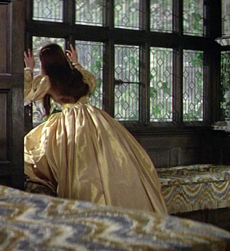 a woman in a yellow dress is sitting on a bed and looking out the window