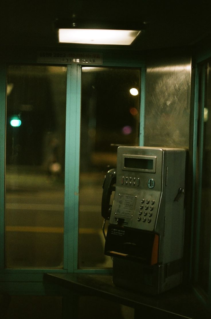 an old pay phone sitting in front of a window with the light shining on it