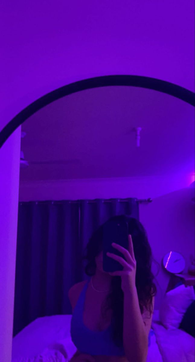 a woman taking a selfie in front of a mirror with purple light on it