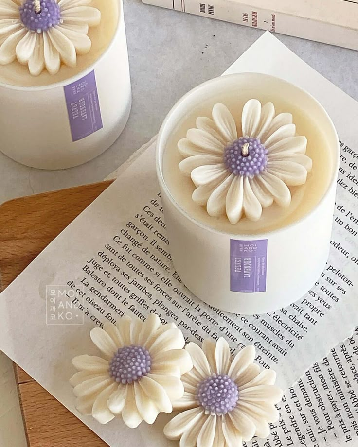 two white candles with purple centers on top of an open book next to some flowers