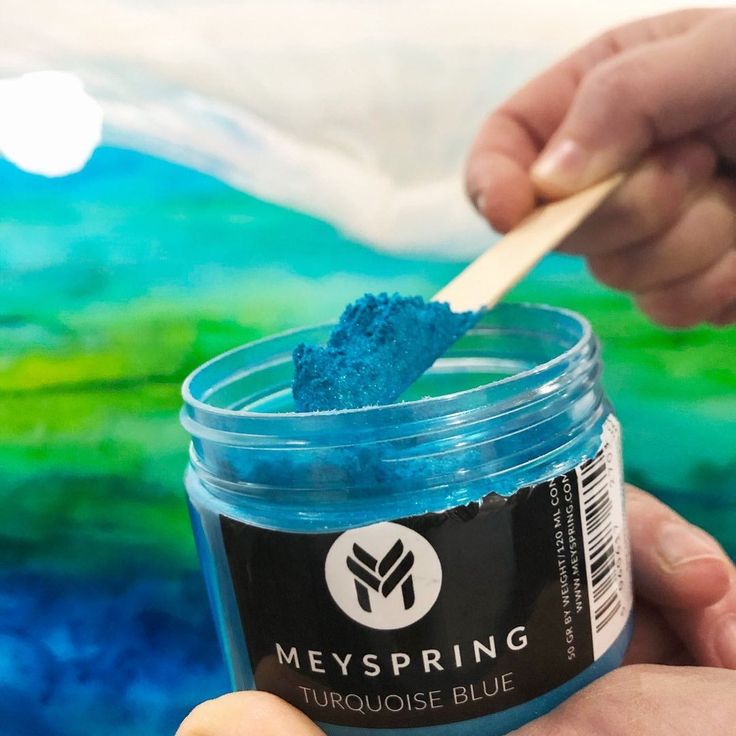 a person holding a wooden spoon over a jar of blue paint