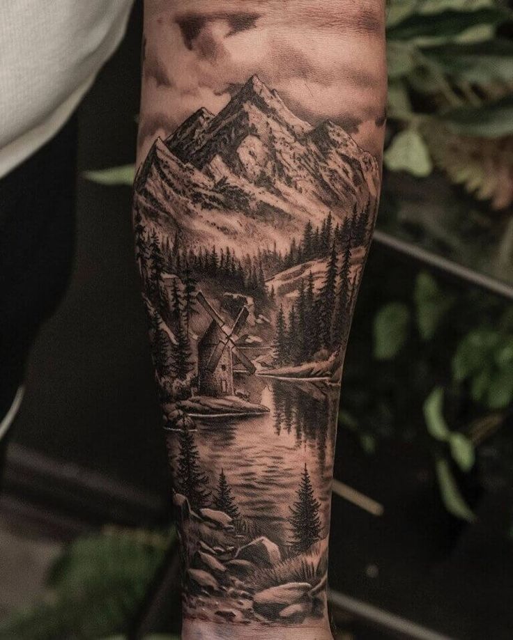 a man's arm with a mountain scene on it and water in the foreground