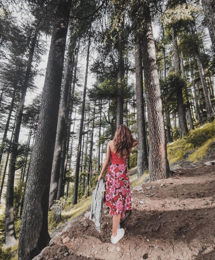 a woman in a red dress is walking through the woods