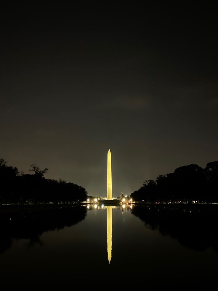 the washington monument is lit up at night with lights reflecting off it's surface