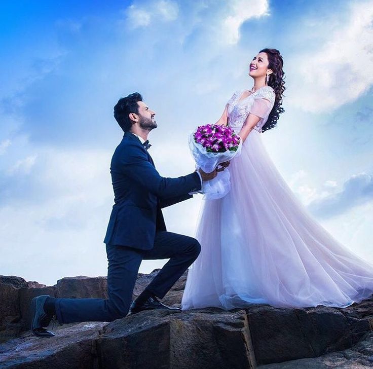 a man kneeling down next to a woman in a wedding dress on top of rocks