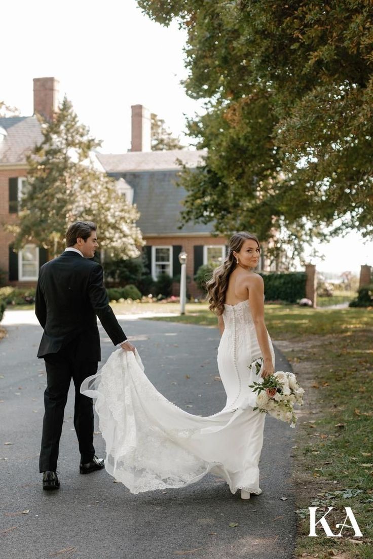 a bride and groom walking down the street holding each other's hands in front of a large house