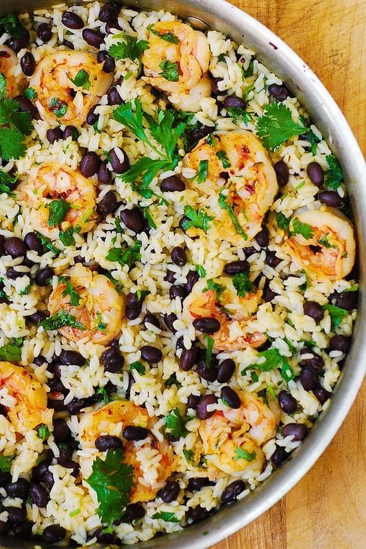 rice with shrimp and black beans in a pan on a wooden table, garnished with parsley