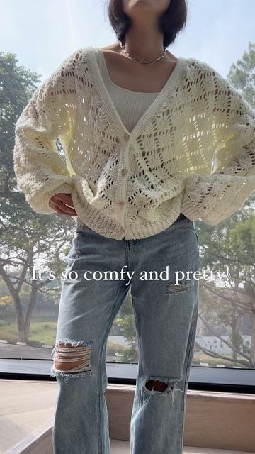 a woman standing in front of a window wearing ripped jeans and a white knitted sweater