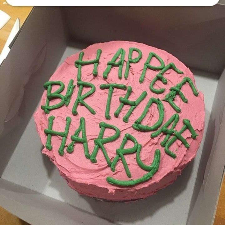 a pink birthday cake with green frosting in a box on top of a table