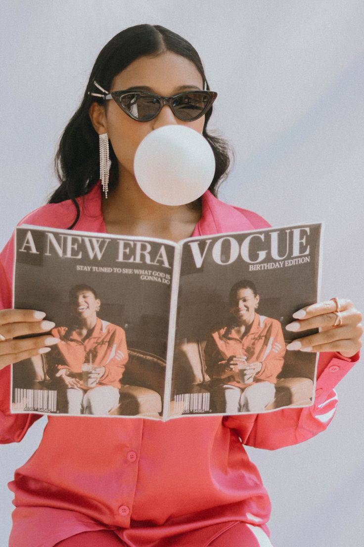 a woman in pink is blowing a bubble while reading a magazine