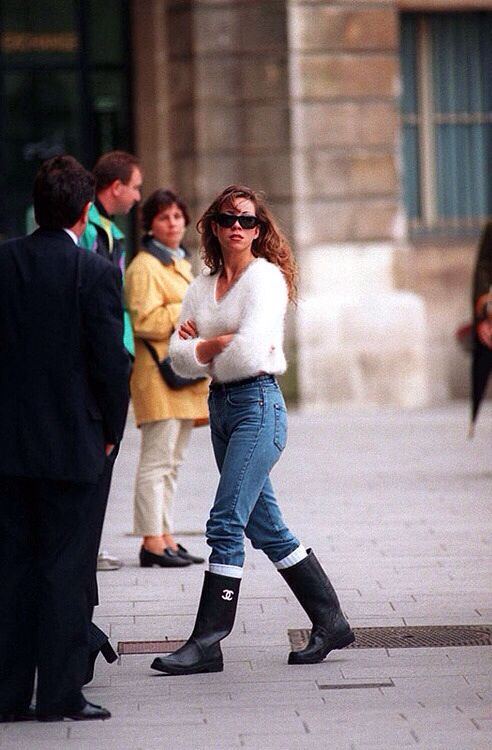 a woman in white sweater and jeans walking on sidewalk with other people behind her wearing black boots