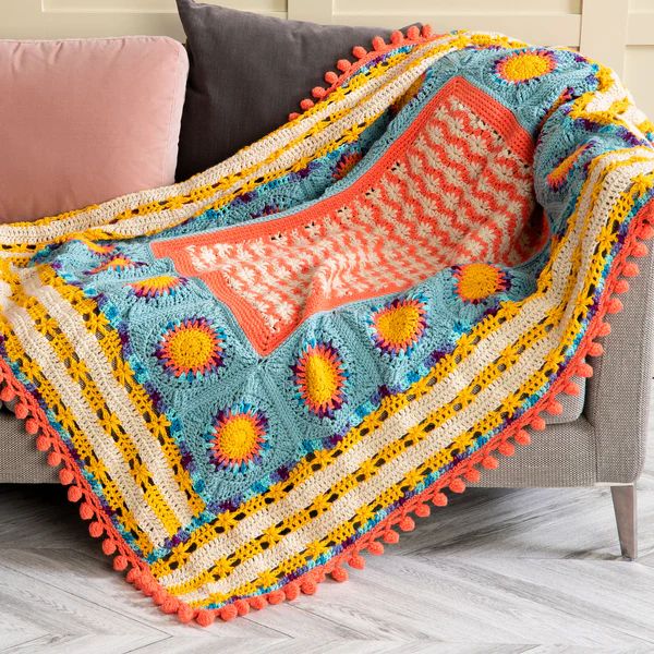 a crocheted blanket is sitting on a couch in front of a pink pillow