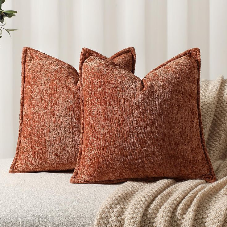 two orange pillows sitting on top of a white couch next to a vase with flowers