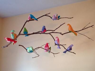 a branch with colorful birds on it hanging from the ceiling in a room that is painted white