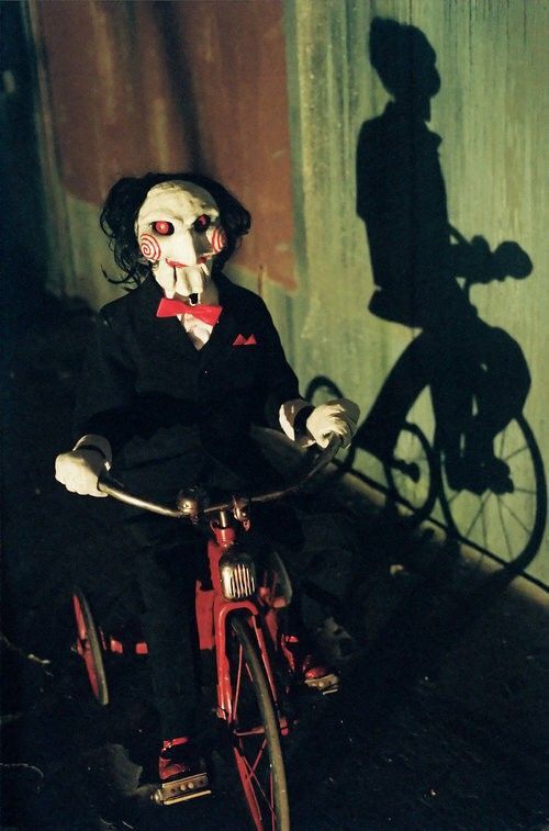 a creepy doll is riding a bike with a shadow of a man on it's face