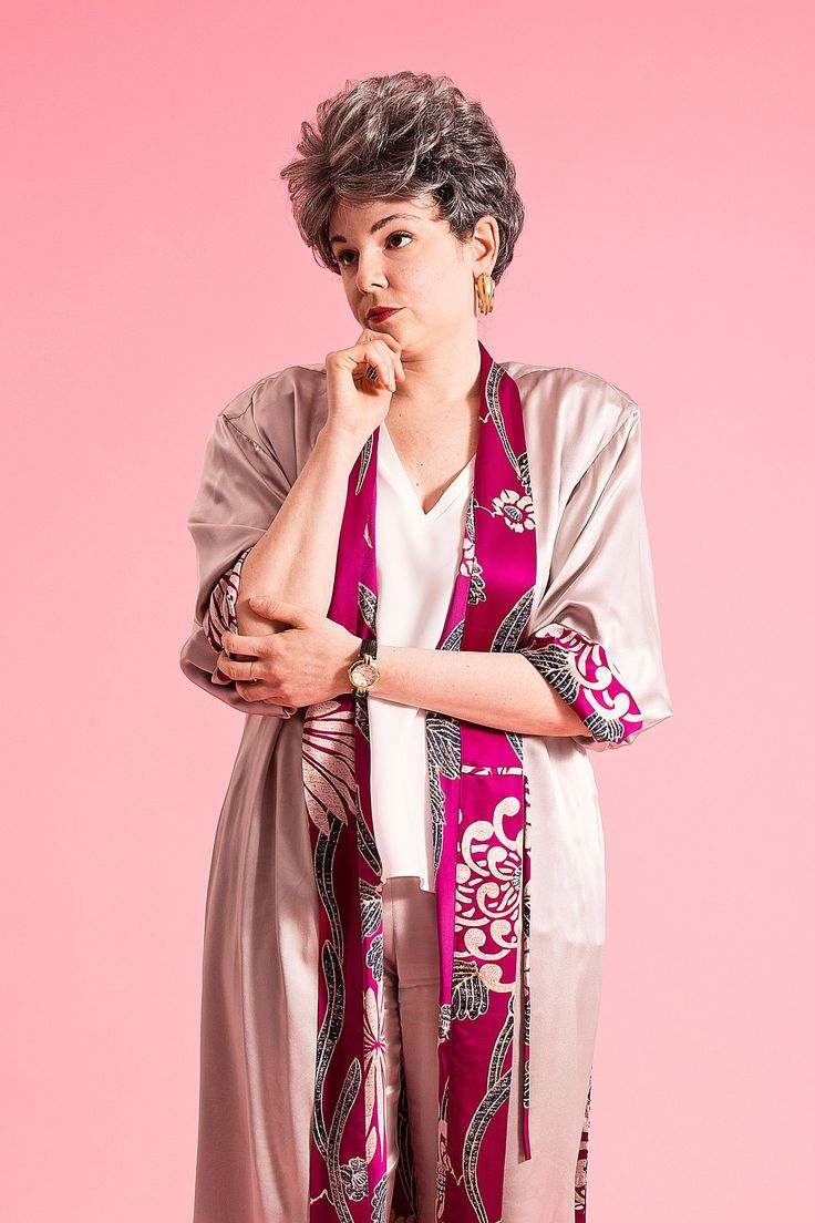 a woman wearing a pink and white scarf with her hand on her chin, standing against a pink background