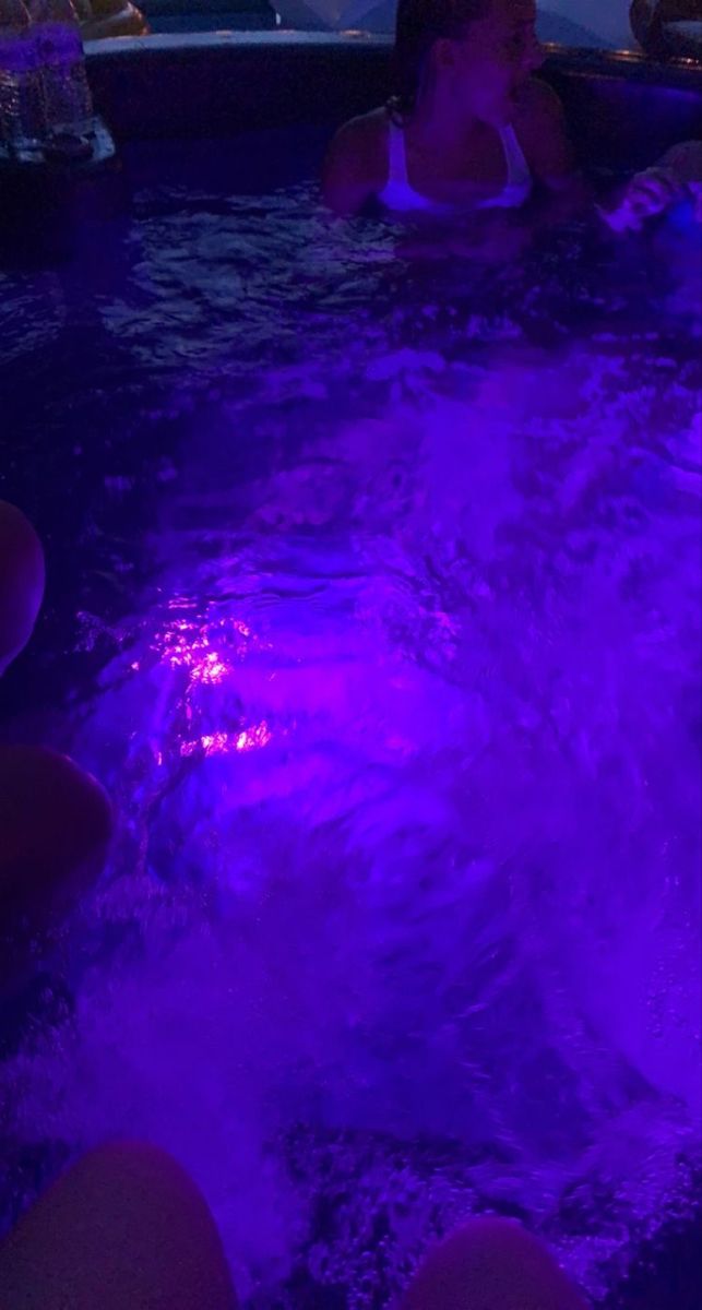 two women sitting in a hot tub with purple lights on the sides and water around them