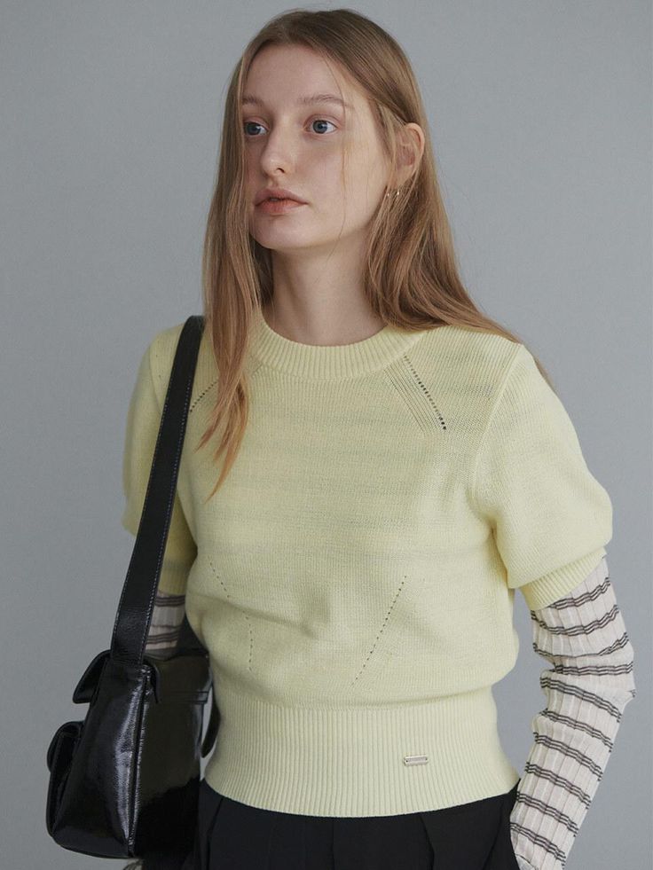 a woman in a yellow sweater is holding a black bag