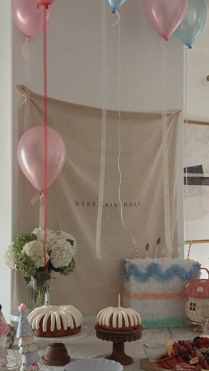 some balloons are hanging from the ceiling above cakes and desserts on a table with flowers in vases