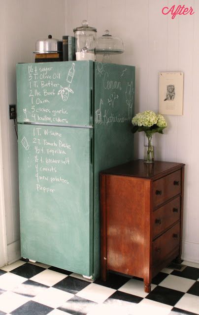 a green refrigerator sitting next to a wooden dresser in a white walled room with chalk writing on the door