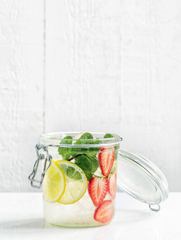 a mason jar filled with sliced strawberries, limes and lemon wedges on a white surface