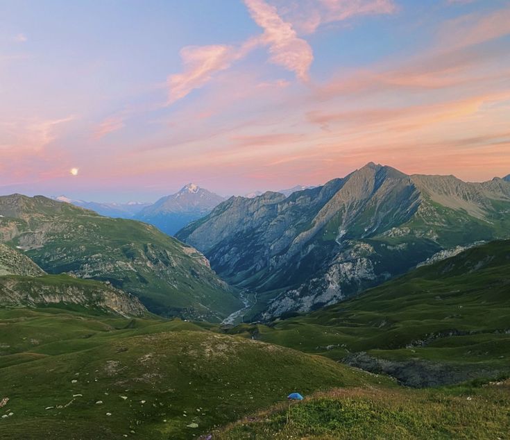 the mountains are covered in green grass as the sun sets