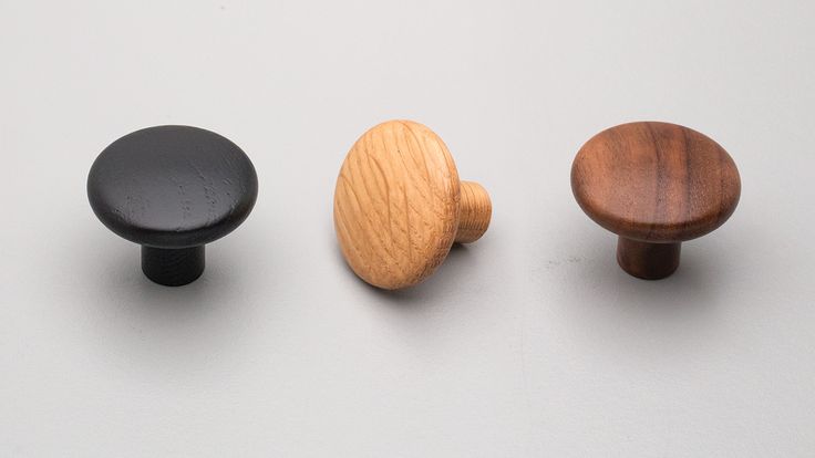 three wooden knobs are shown on a white surface, one is black and the other is wood