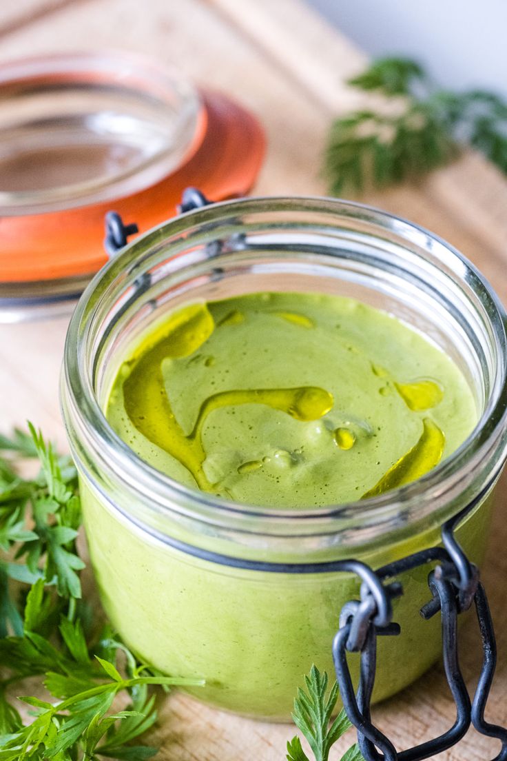 a jar filled with green liquid sitting on top of a wooden cutting board next to parsley