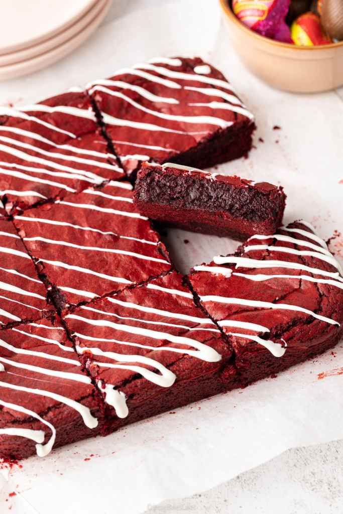 red velvet brownies with white icing and chocolate candies on the side, ready to be eaten