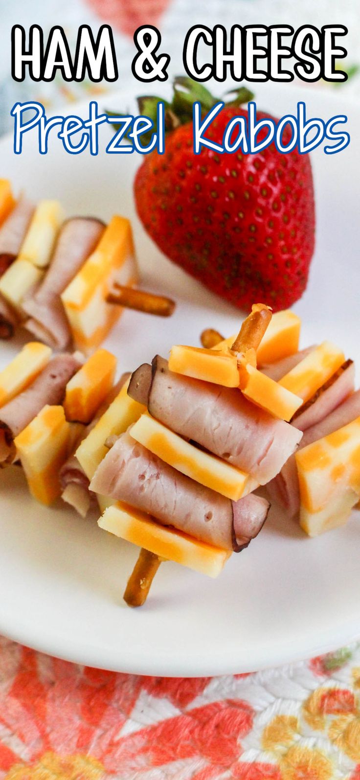 ham and cheese pretzel kabobs on a white plate with strawberries