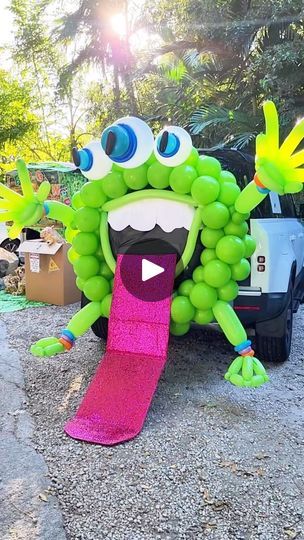 an inflatable green monster holding a pink skateboard on the side of a road