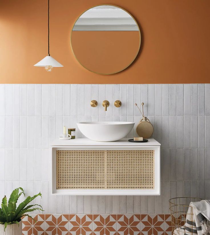 a white sink sitting under a round mirror next to a potted plant on top of a counter